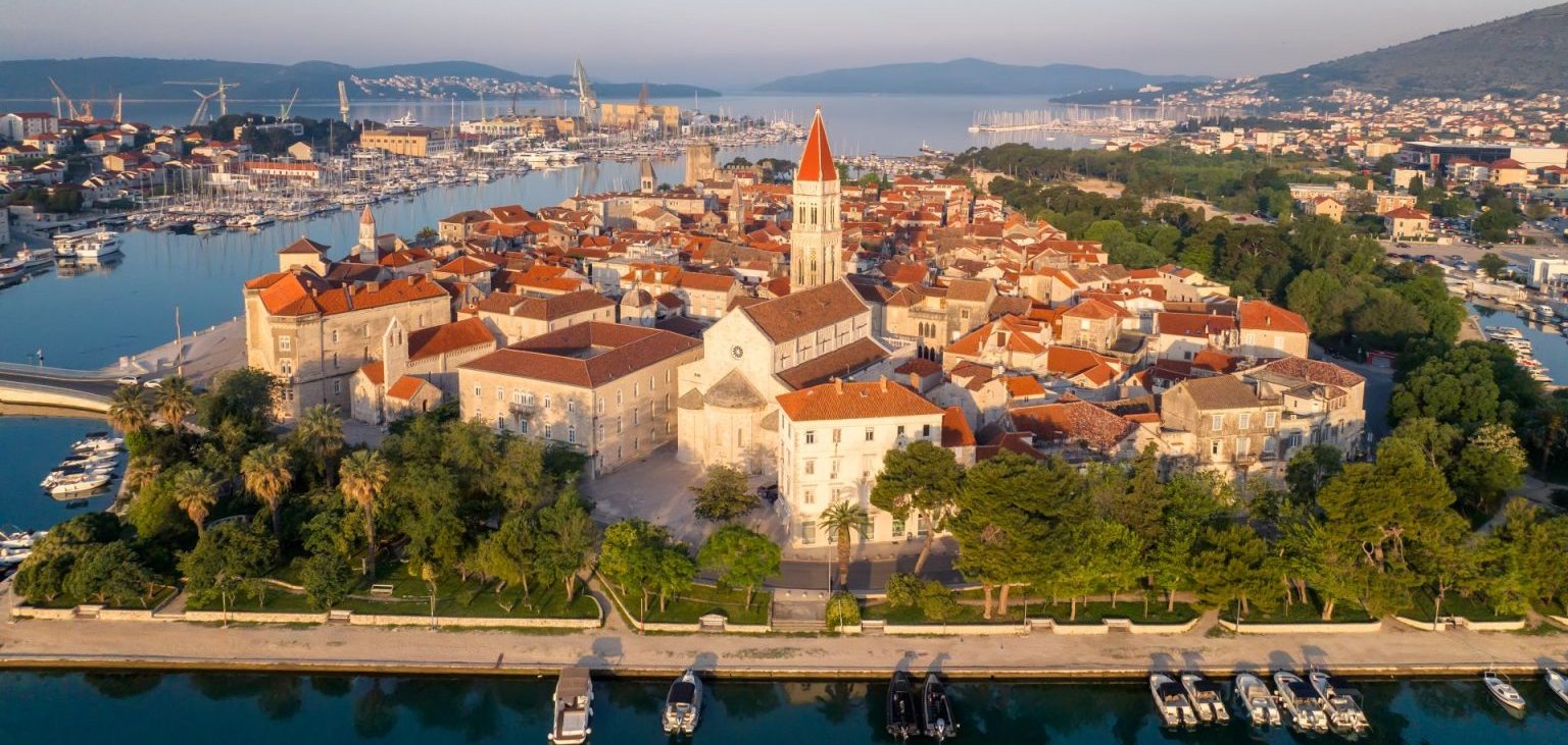 Aerial view of Trogir old town on the Dalmatian coast, its terracotta roofs ringed by water, with the marina and Čiovo island beyond